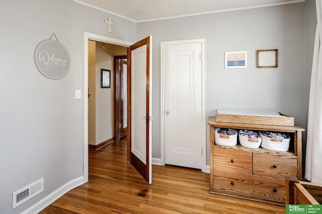 corridor featuring visible vents, crown molding, baseboards, and wood finished floors