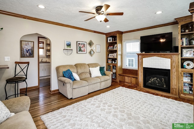 living area with baseboards, ornamental molding, wood finished floors, arched walkways, and a textured ceiling