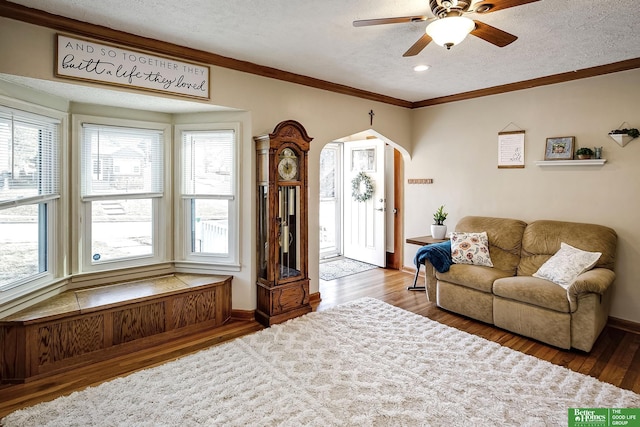 living area with baseboards, ornamental molding, wood finished floors, arched walkways, and a textured ceiling