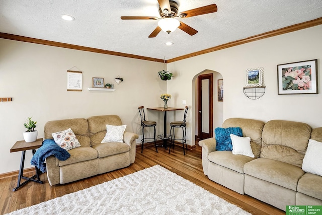 living area featuring wood finished floors, arched walkways, ceiling fan, a textured ceiling, and crown molding