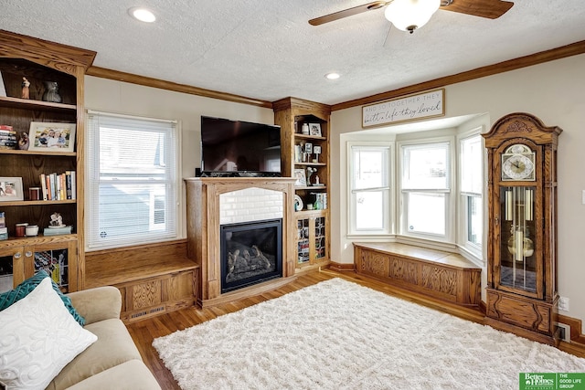 living room with visible vents, ornamental molding, a textured ceiling, wood finished floors, and a fireplace