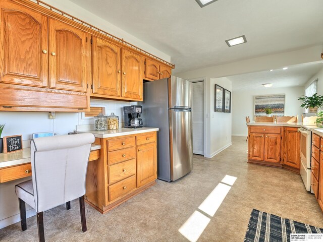 kitchen with white range with electric stovetop, freestanding refrigerator, brown cabinetry, light countertops, and light floors