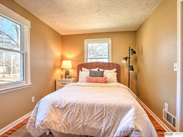 bedroom with visible vents, a textured ceiling, baseboards, and wood finished floors