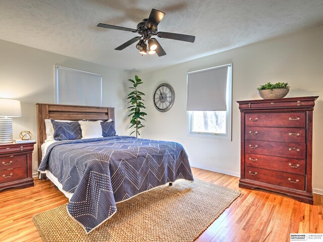 bedroom with ceiling fan, baseboards, light wood-type flooring, and a textured ceiling