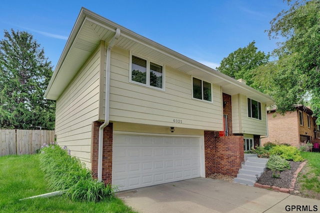 bi-level home featuring a garage, brick siding, driveway, and fence