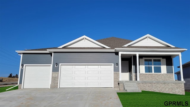 view of front of house with a front yard, roof with shingles, an attached garage, concrete driveway, and stone siding