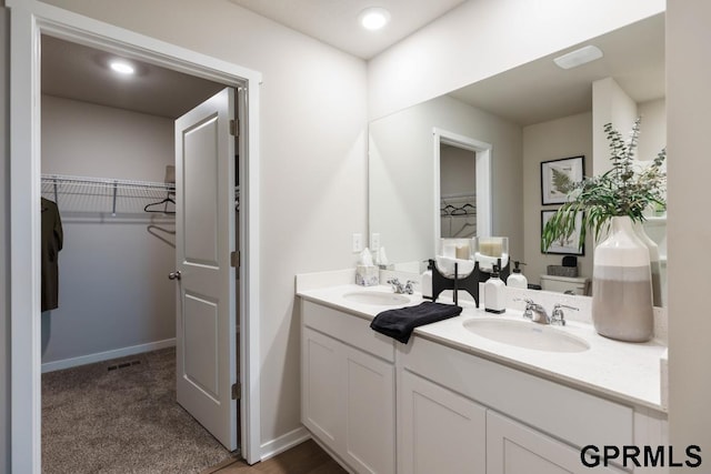 full bath with vanity, a spacious closet, visible vents, and baseboards