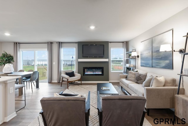 living room featuring a glass covered fireplace, recessed lighting, baseboards, and wood finished floors