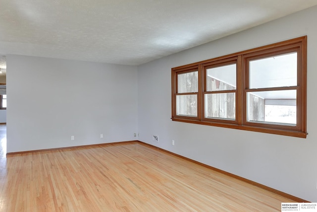 spare room with visible vents, light wood-style flooring, a textured ceiling, and baseboards