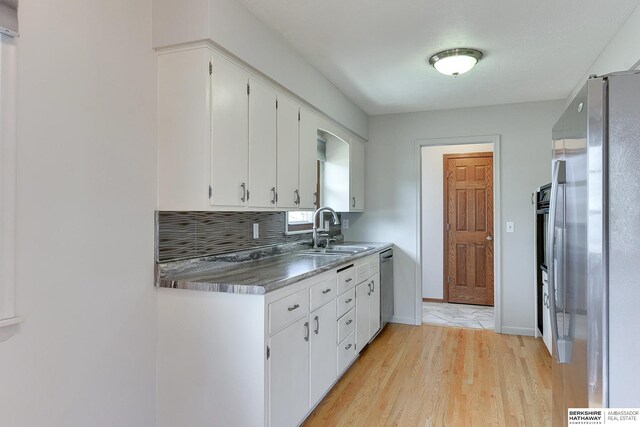 kitchen featuring light wood-style flooring, a sink, white cabinets, appliances with stainless steel finishes, and tasteful backsplash