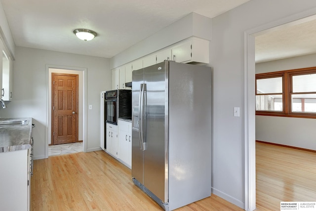 kitchen with light wood finished floors, stainless steel fridge, white cabinetry, and baseboards