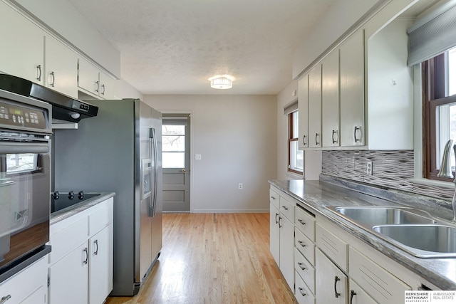 kitchen featuring light wood finished floors, a sink, black appliances, white cabinets, and backsplash