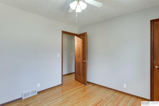 empty room with baseboards, visible vents, light wood finished floors, and a textured ceiling