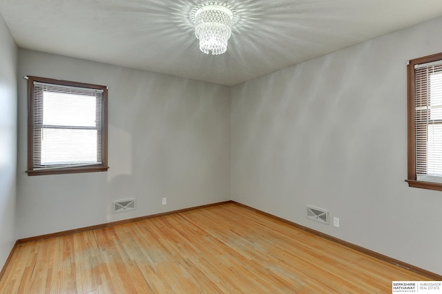 empty room with a healthy amount of sunlight, visible vents, a chandelier, and light wood-type flooring