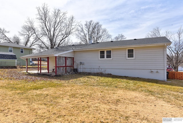 rear view of house with a carport, a lawn, a shingled roof, and fence