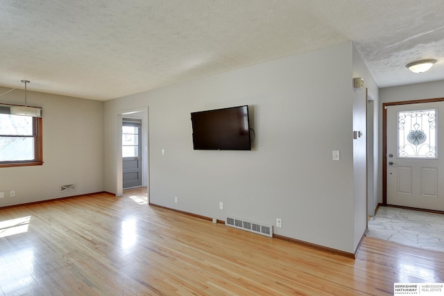 unfurnished living room featuring light wood-style flooring, baseboards, visible vents, and a textured ceiling