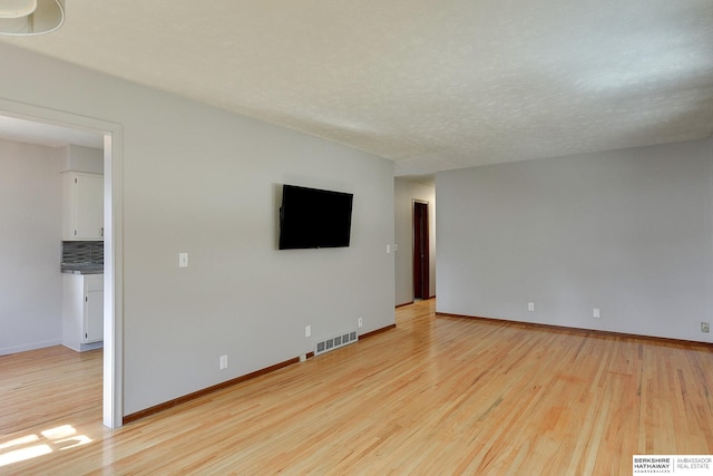 unfurnished living room with visible vents, a textured ceiling, light wood-type flooring, and baseboards