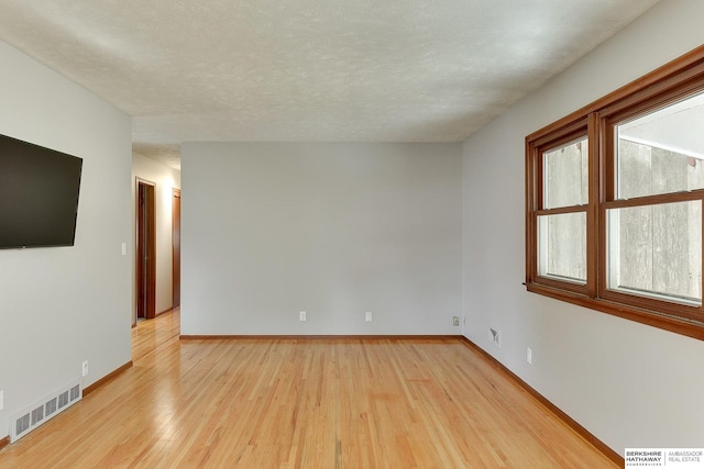 empty room featuring visible vents, baseboards, light wood-style floors, and a textured ceiling