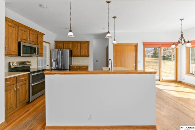 kitchen featuring decorative light fixtures, light countertops, light wood-type flooring, brown cabinets, and appliances with stainless steel finishes