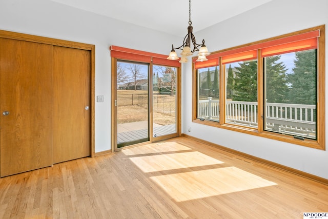 unfurnished dining area featuring baseboards, an inviting chandelier, and wood finished floors