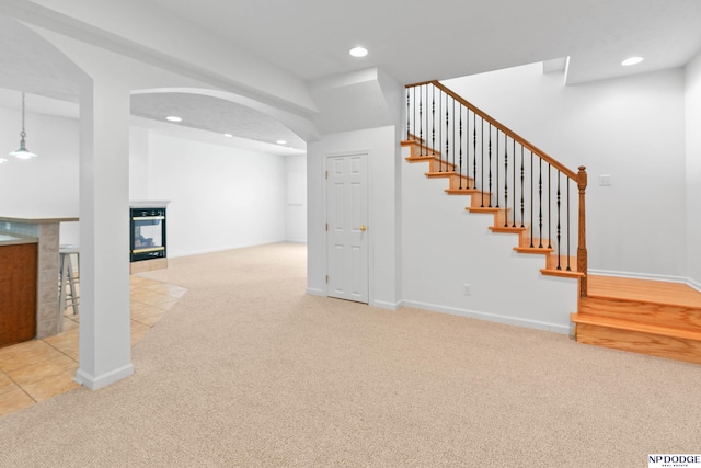 below grade area featuring a tiled fireplace, carpet flooring, recessed lighting, and stairs