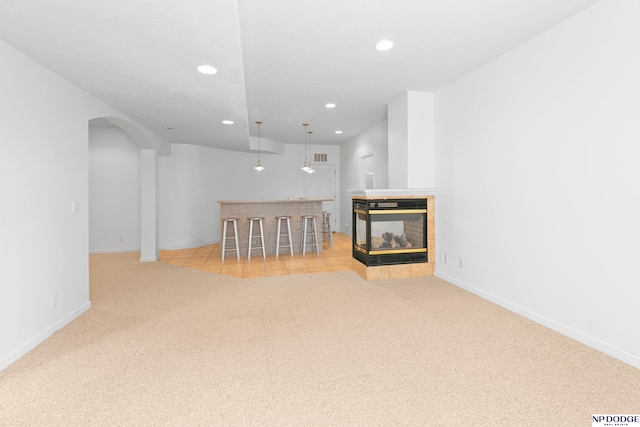 unfurnished living room with baseboards, recessed lighting, arched walkways, a multi sided fireplace, and light carpet