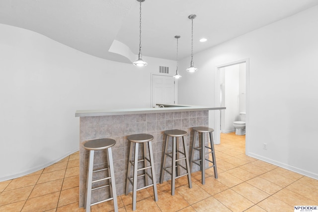 kitchen featuring visible vents, baseboards, pendant lighting, a kitchen bar, and light tile patterned flooring