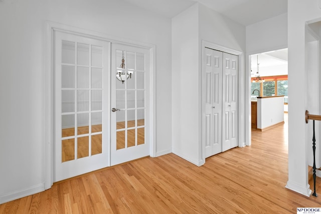 interior space featuring baseboards, light wood finished floors, a sink, french doors, and a notable chandelier