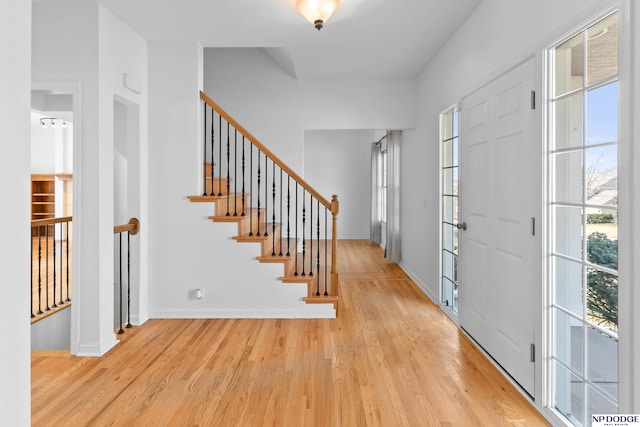 foyer entrance featuring light wood finished floors, stairs, and baseboards