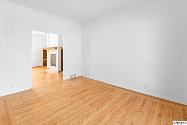 spare room featuring visible vents, baseboards, a tiled fireplace, light wood-type flooring, and ornamental molding