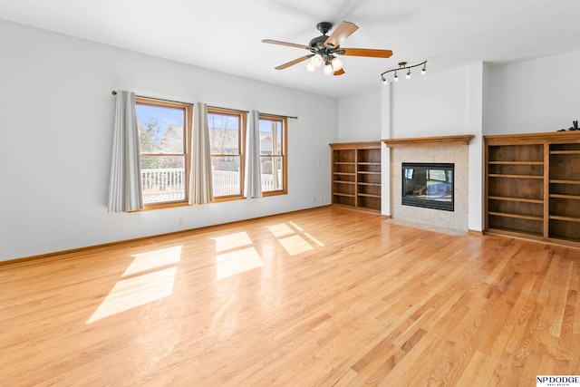 unfurnished living room with baseboards, a ceiling fan, wood finished floors, and a tiled fireplace