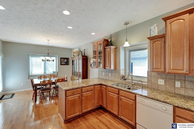 kitchen featuring light wood finished floors, dishwasher, a peninsula, and a sink