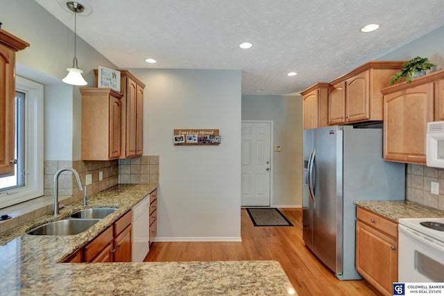 kitchen with light stone countertops, decorative light fixtures, light wood-type flooring, white appliances, and a sink