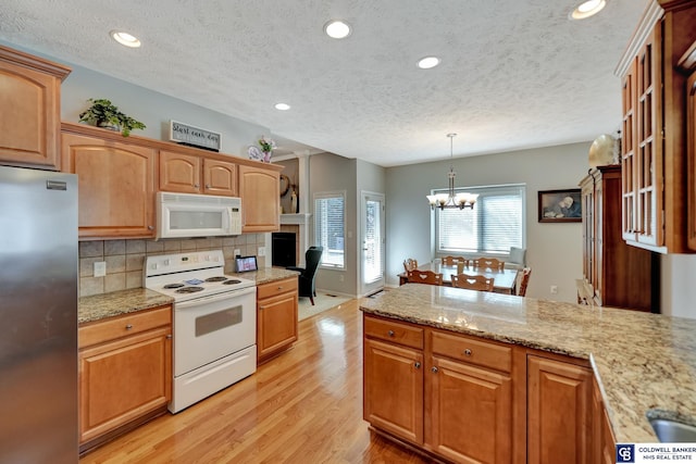 kitchen featuring light wood-type flooring, decorative light fixtures, tasteful backsplash, white appliances, and a peninsula