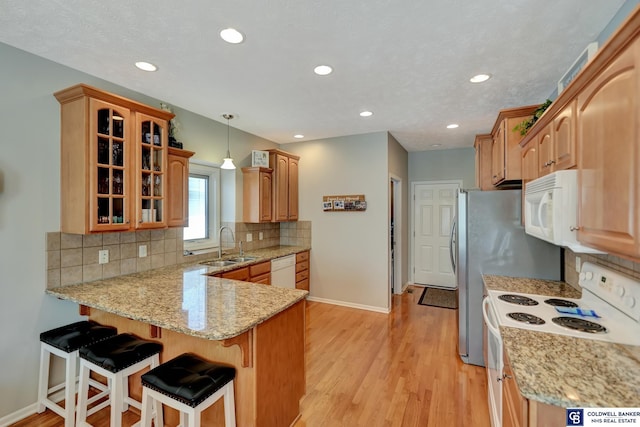 kitchen featuring glass insert cabinets, a breakfast bar area, a peninsula, white appliances, and a sink