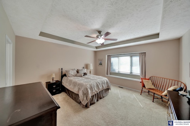 bedroom featuring visible vents, light carpet, a textured ceiling, a raised ceiling, and ceiling fan