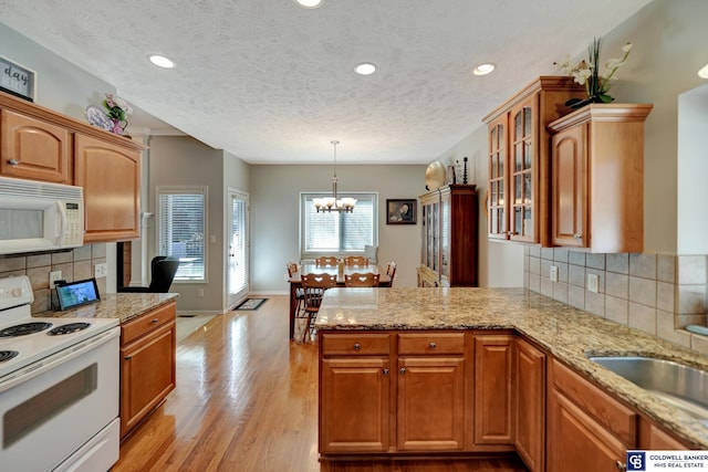 kitchen with white appliances, light stone countertops, a peninsula, glass insert cabinets, and light wood-style floors