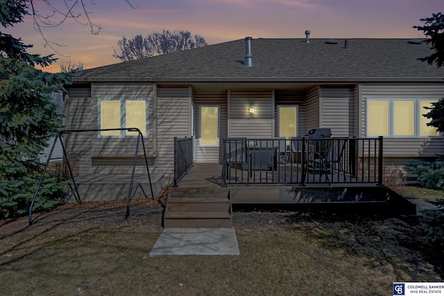 back of house at dusk featuring a wooden deck and a shingled roof