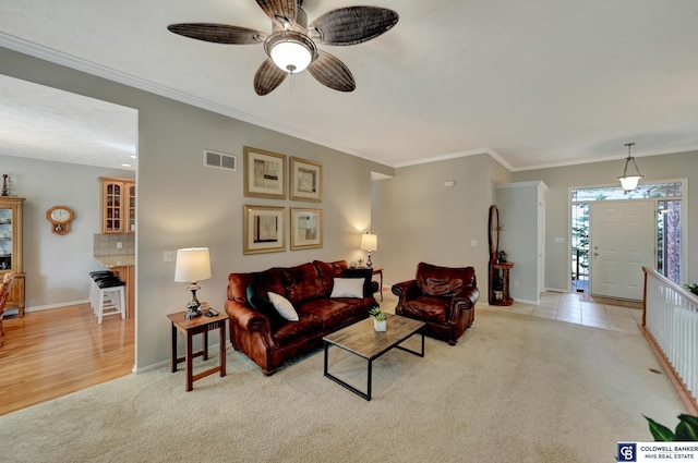 living area featuring visible vents, light carpet, ornamental molding, baseboards, and ceiling fan