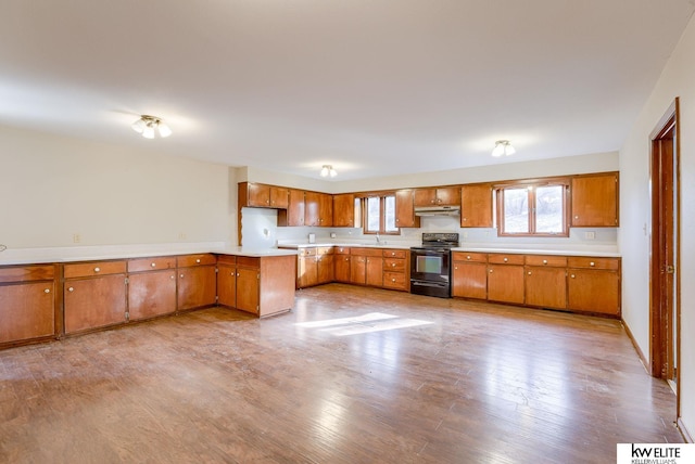 kitchen with wood finished floors, brown cabinetry, electric range, a sink, and under cabinet range hood