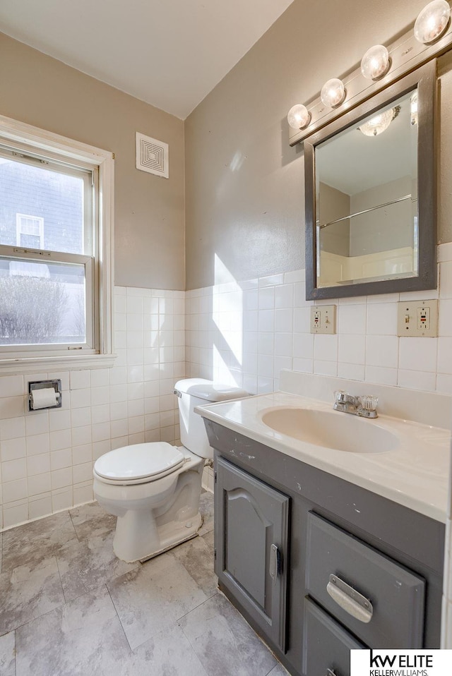 bathroom with vanity, visible vents, wainscoting, tile walls, and toilet