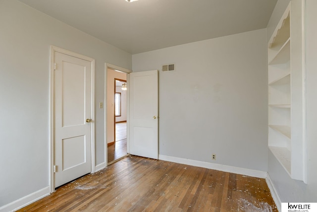 empty room featuring hardwood / wood-style floors, baseboards, and visible vents