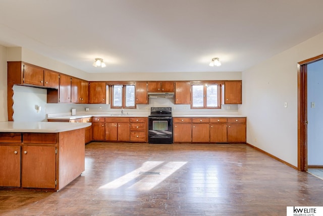 kitchen featuring a sink, under cabinet range hood, black range with electric cooktop, brown cabinetry, and light countertops