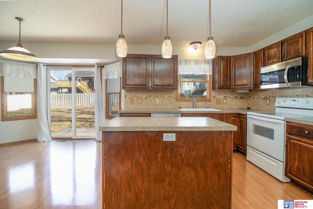 kitchen featuring white range with electric cooktop, a sink, stainless steel microwave, a center island, and decorative backsplash