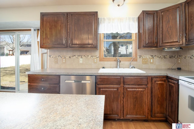 kitchen featuring a sink, backsplash, light countertops, and stainless steel dishwasher