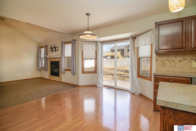 unfurnished living room with lofted ceiling, light wood-style floors, baseboards, and a tile fireplace