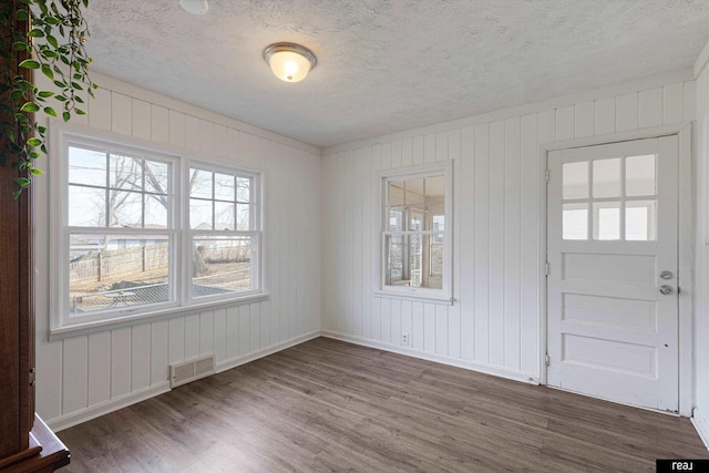 interior space with visible vents, a textured ceiling, baseboards, and wood finished floors