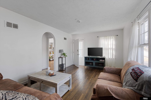 living area featuring plenty of natural light, arched walkways, visible vents, and dark wood-style flooring