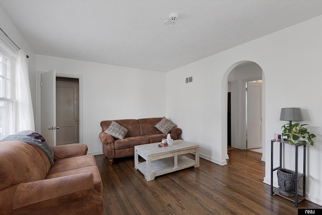 living room with arched walkways, visible vents, dark wood-type flooring, and baseboards