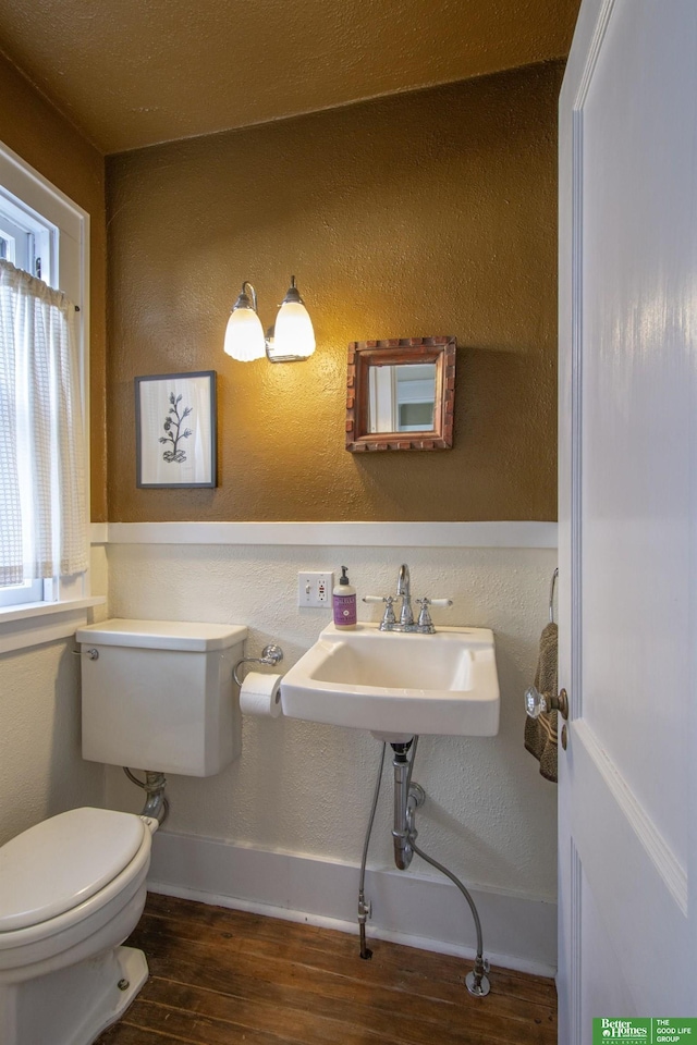 half bathroom featuring baseboards, toilet, wood finished floors, and a textured wall